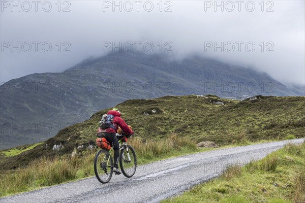 Lonely biker cycling through the Scottish Highlands on heavily laden touring bicycle along single