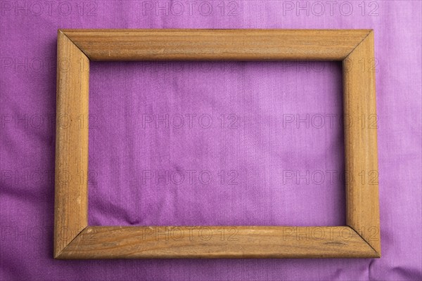 Wooden frame on smooth cotton purple tissue. Top view, flat lay, natural textile background and