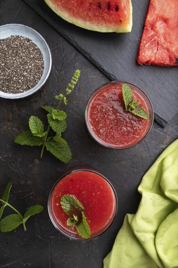 Watermelon juice with chia seeds and mint in glass on a black concrete background with green