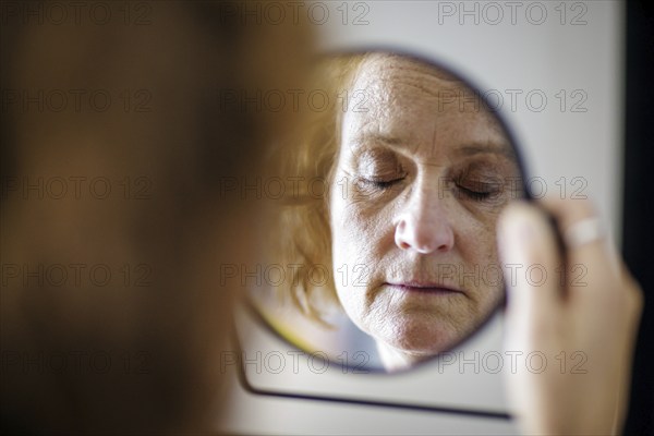 Symbol photo. An elderly woman with closed eyes can be seen in a mirror. Berlin, 13.08.2024