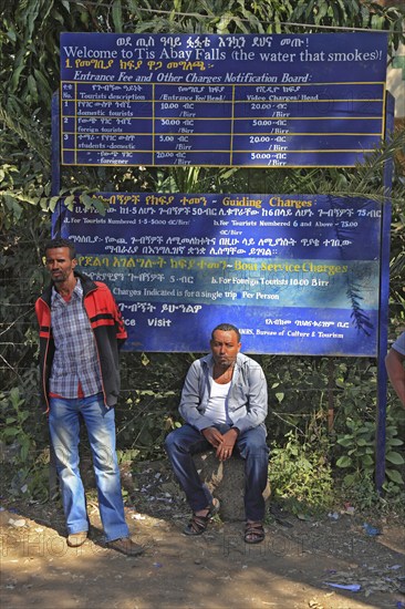 Two locals in front of the price board with the fares for the trip to Abay Falls, Ethiopia, Africa