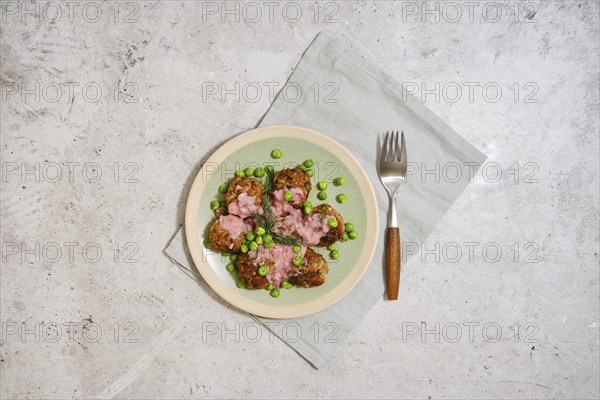 Top view of meatballs with fresh green peas and cranberry sauce on grey stone background