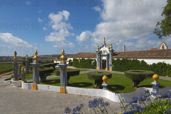 Traditional building in a well-kept garden with hedges and decorative elements under a sky with