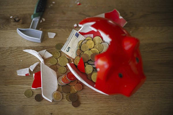 Symbolic photo on the subject of saving. An open, broken piggy bank with coins and banknotes stands