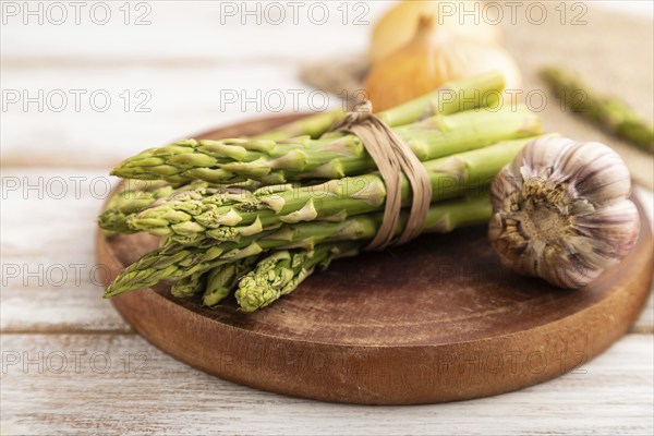 Bunch of fresh green asparagus, garlic, onion on white wooden background. Side view, selective