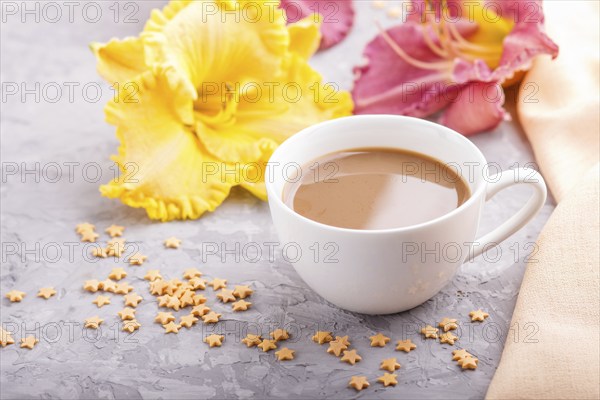 Yellow anf purple day-lilies cup of coffee on a gray concrete background, with orange textile.