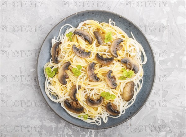 Rice noodles with champignons mushrooms, egg sauce and oregano on blue ceramic plate on a gray