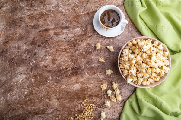 Popcorn with caramel in ceramic bowl on brown concrete background and green textile. Top view, flat