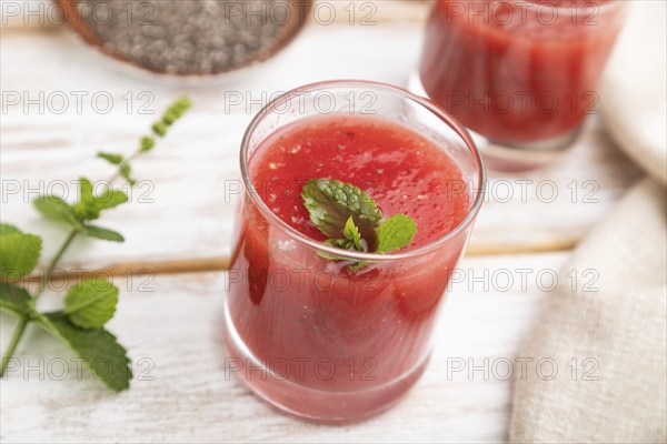 Watermelon juice with chia seeds and mint in glass on a white wooden background with linen textile.