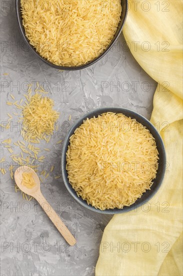 Blue ceramic bowl with raw golden rice and wooden spoon on a gray concrete background and yellow
