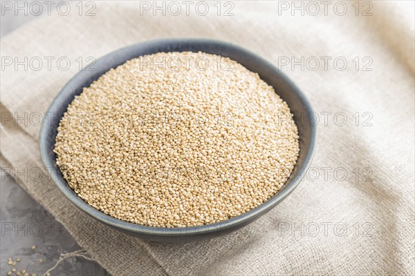 Blue ceramic bowl with raw white quinoa seeds on a gray concrete background and linen textile. Side