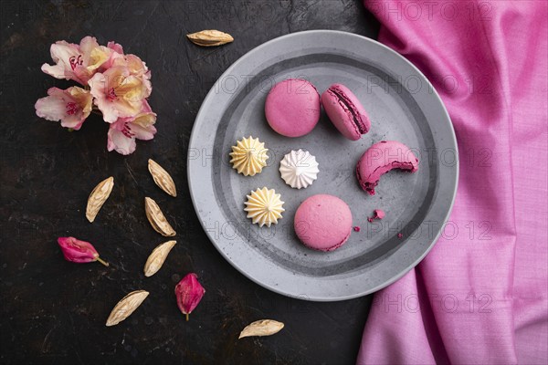 Purple macarons or macaroons cakes with cup of coffee on a black concrete background and pink
