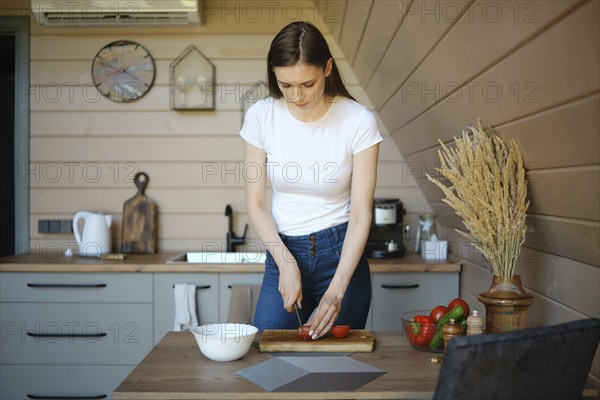 Young woman slicing fresh tomato on wooden chopping board in a wooden kitchen