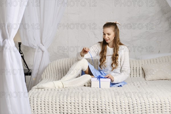 Young woman unpacking a gift, she pulls the ribbon while sitting on bed