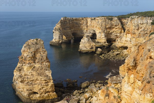 Large, eroded cliffs and rocks stretch along a coastline with calm seas and clear skies, Praia da