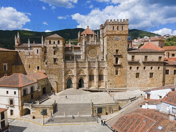 Aerial view of the facade of a monastery with red roofs and wide stairs under a blue sky in Spain.