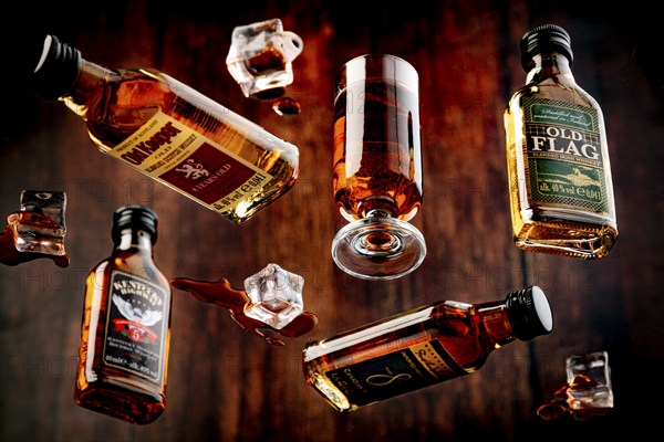 Four whisky bottles and a glass with spilt whisky and melted ice against a wooden background