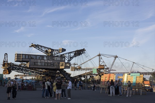 Festival visitors in front of open-cast mining excavator and Melt logo at the Melt Festival in