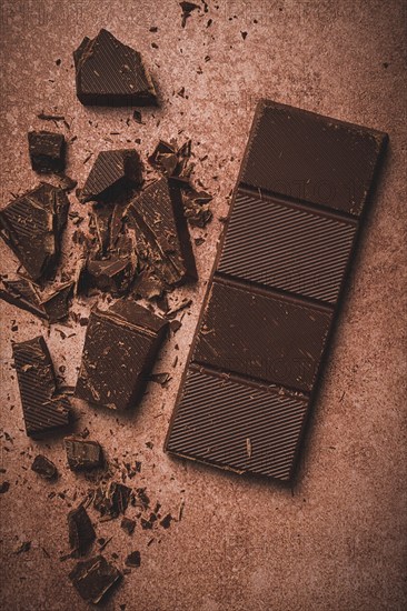 Chocolate bar, for the manufacture of confectionery, broken, crumbled, on a brown background, top