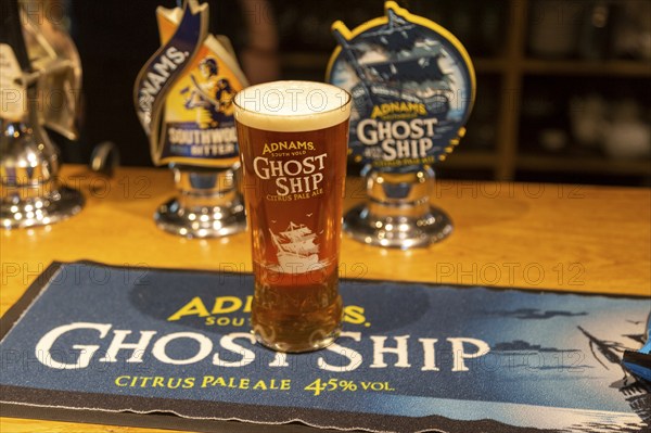 Pint glass of Adnams Ghost Ship Citrus pale Ale, on beer mat with bar pumps, Suffolk, UK