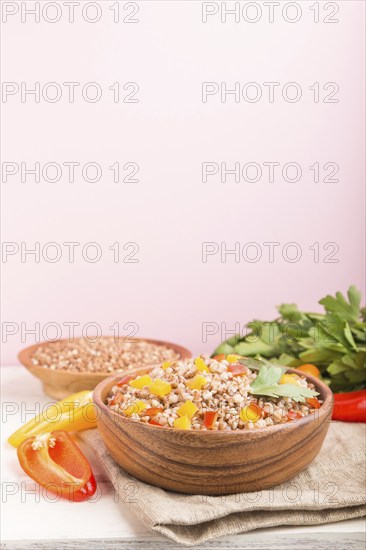 Buckwheat porridge with vegetables in wooden bowl on a pink background and linen textile. Side