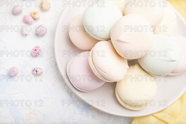 Colored zephyr or marshmallow and dragees on white concrete background and yellow textile. top