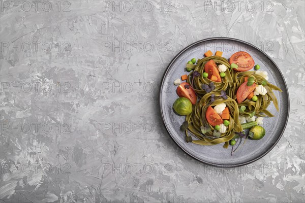 Tagliatelle green spinach pasta with tomato, pea and microgreen sprouts on a gray concrete