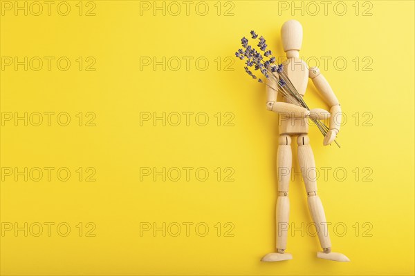 Wooden mannequin holding lavender flowers on yellow pastel background. copy space, isolated,