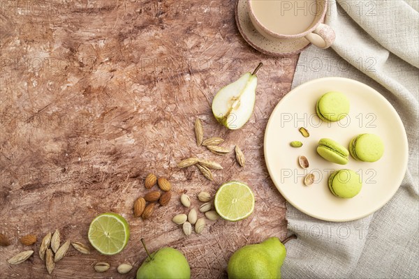 Green macarons or macaroons cakes with cup of coffee on a brown concrete background and linen
