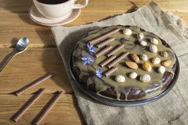 Homemade chocolate brownie cake with caramel cream and almonds with cup of coffee on wooden
