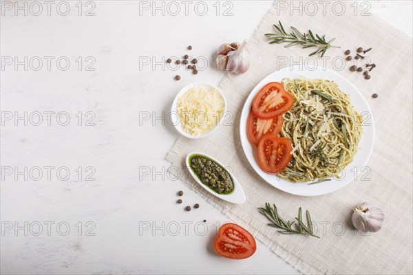Spaghetti pasta with pesto sauce, tomatoes and cheese on a linen tablecloth on white wooden