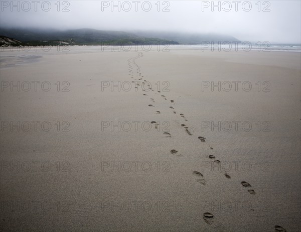 Foot step prints in wet sand on a cloudy overcast day at Traigh Eais beach, Barra, Outer Hebrides,