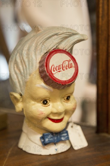 Old vintage Coca Cola advertising sign in form of boy's head inside antiques centre, Marlesford