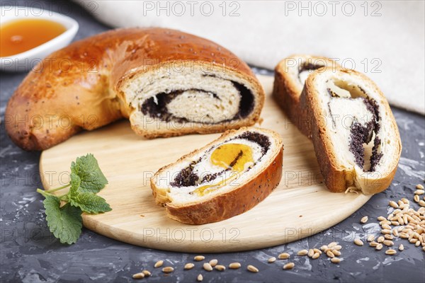 Homemade yeast rolls with poppy seeds and honey on a wooden kitchen board on a black concrete
