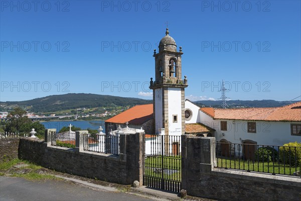 Church with bell tower and closed entrance gate, in the background a hilly landscape and blue sky,