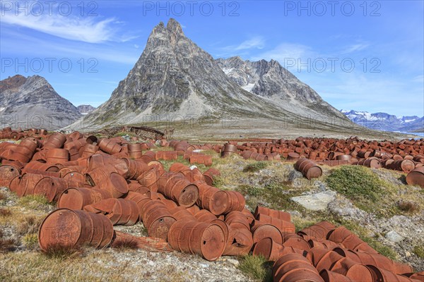 Rusted oil barrels on a fjord in front of steep mountains, remains of a US airbase from the Second