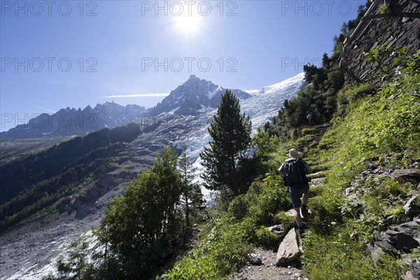 Hiker on hiking trail La Jonction, view of glacier Glacier des Bossons with sun star, behind summit
