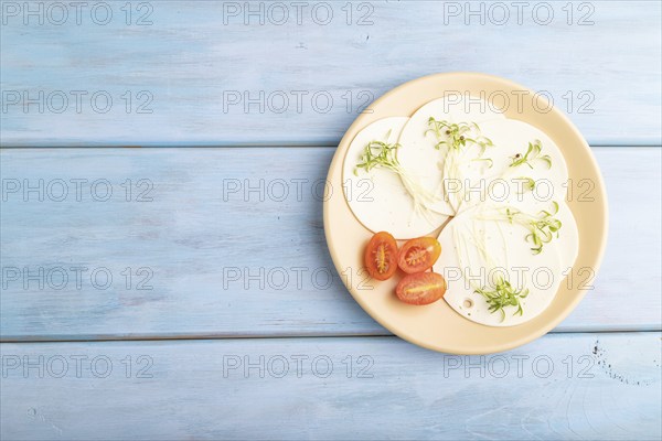 White cheese with tomatoes and cilantro microgreen on blue wooden background. top view, flat lay,