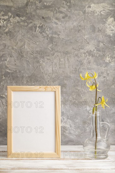 Wooden frame with yellow trout lily or dogtooth violet flowers in glass on gray concrete background