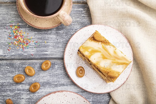 Honey cake with milk cream, caramel, almonds and a cup of coffee on a gray wooden background and