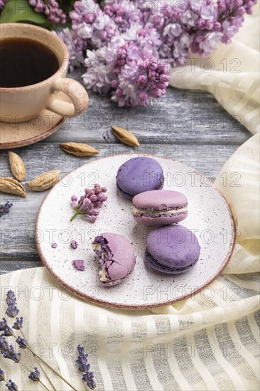 Purple macarons or macaroons cakes with cup of coffee on a gray wooden background and white linen