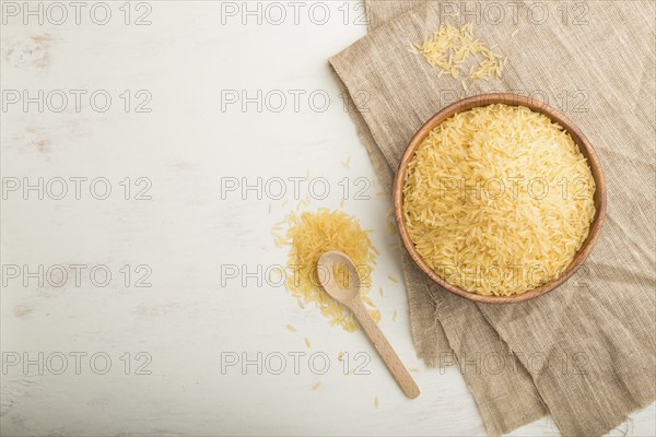 Wooden bowl with raw golden rice and wooden spoon on a white wooden background and linen textile.
