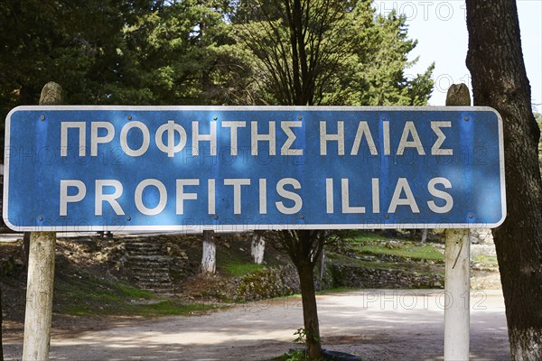 Street sign with Greek and Latin text 'Profitis Ilias' in a natural forest landscape, Profitis