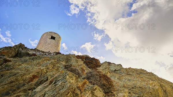 Ruin of a windmill, Old tower on a rocky hill in front of a cloudy sky, Colourful mountain village,