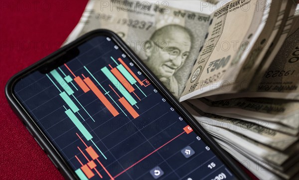 Stock market graph or chart display on a mobile phone against Indian 500 rupee paper currency note
