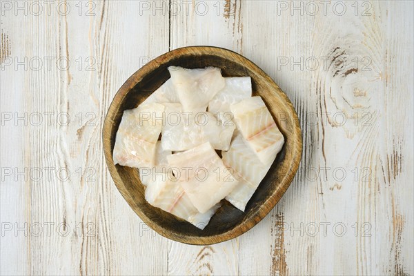 A wooden bowl filled with fresh, cut pieces of white fish fillet sits on a rustic wooden tabletop,