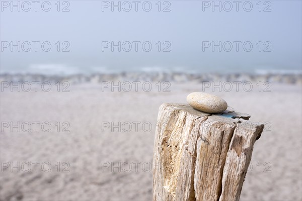 A single stone lies on a wooden pole on the beach with foggy background, pebble on pole, sandy