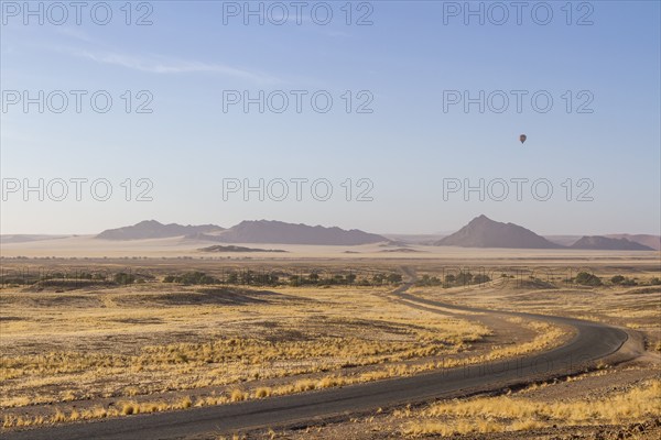 Landscape in arid environment with a road, mountains in the background and a hot air balloon in the