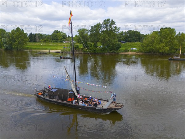 A boat sails with passengers on a calm river, surrounded by green landscape and trees under a