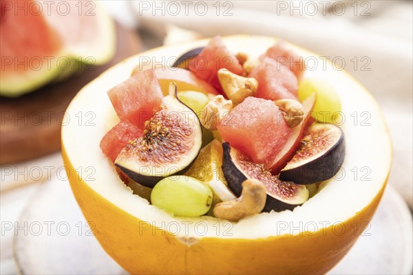 Vegetarian fruit salad of watermelon, grapes, figs, pear, orange, cashew on white wooden background